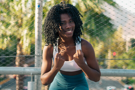 bella mujer negra optimista y sonriendo despu&eacute;s de correr y hacer ejercicios en un d&iacute;a de sol en la ciudad.