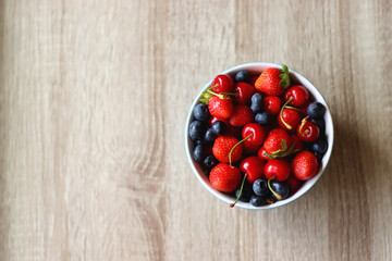 Bowl filled with fresh blueberries, cherries and strawberries on wooden table. Top view.