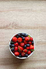 Bowl filled with fresh blueberries, cherries and strawberries on wooden table. Top view.