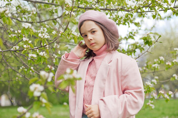Portrait of adorable little girl stands in a blooming white apple tree in the park.