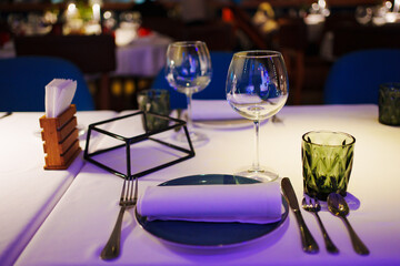 a table with a white tablecloth, glasses, crockery and decor in dark restaurant