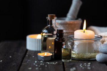 Spa setting with essential oil, candle, sea salt, pebbles, towel on dark wooden background. Massage, aromatherapy. Natural organic ingredients for relaxation, detention. Wellness in salon concept