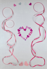 Valentine's or wedding Day greeting card with a frame of wavy pink and magenta ribbons ,decorated with hearts on beige textured background. Top view, flat lay. Free copy space