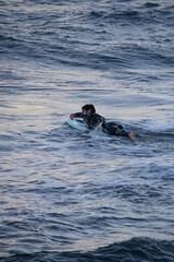 Surfista con neopreno negro nadando mar adentro para surfear