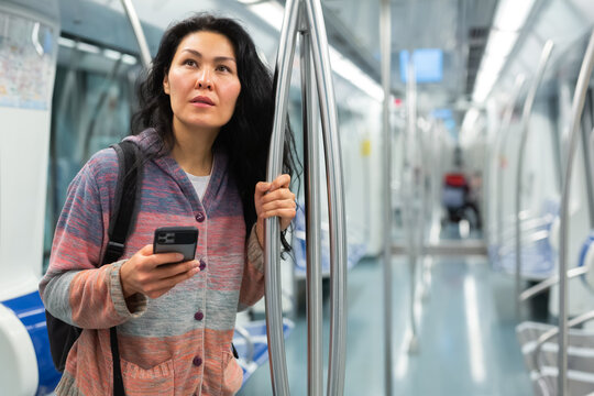 Young adult woman passenger with luggage standing in subway car and using mobile phone