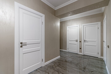 Corridor with white walls and doors in an apartment with a marble floor