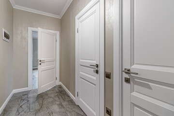 Corridor with white walls and doors in an apartment with a marble floor
