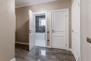 Corridor with white walls and doors in an apartment with a marble floor