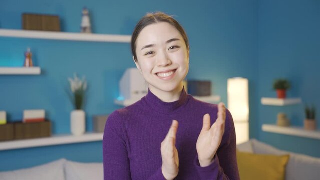 Asian woman happily clapping while looking at camera. 
Cute Asian young woman looking at camera and smiling and clapping.
