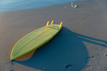 Naklejka premium High angle view of yellow surfboard on sandy beach at shore during sunset