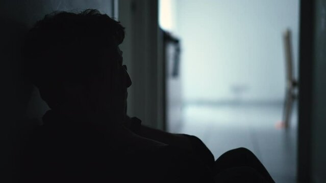 One male person covering face in shame sitting at home floor in the dark during crisis. Person suffering from depression