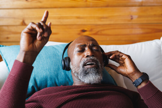 African american senior man listening music and singing while lying on sofa in log cabin