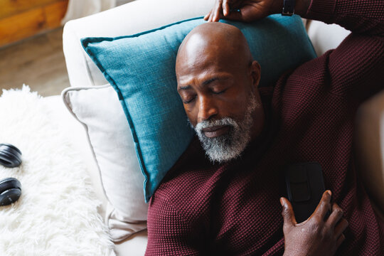 High angle view of bald african american senior man with mobile phone sleeping on couch at log cabin