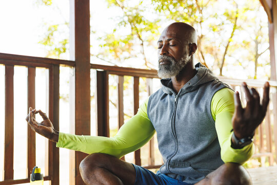 Bald african american senior man with eyes closed meditating in balcony at log cabin - Powered by Adobe