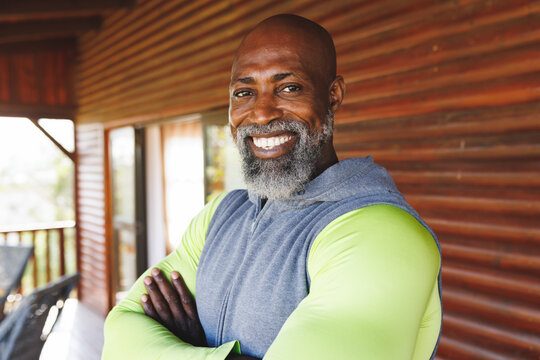 Smiling bald african american senior man with arms crossed standing against wall in log cabin