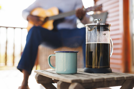 French press and mug on table over midsection of african american senior man playing guitar - Powered by Adobe