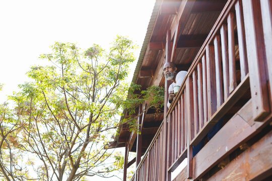 Low angle view of african american thoughtful senior man with coffee mug standing by railing
