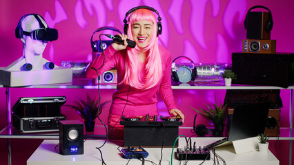 Obraz na płótnie Canvas Dj woman putting headphones before start mixing music using audio equipment during techno party in nightclub. Asian performer with pink hair creating musical performance with mixer console