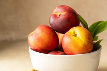 Closeup nectarine peaches, fresh red fruits in a bowl. Neutral background.