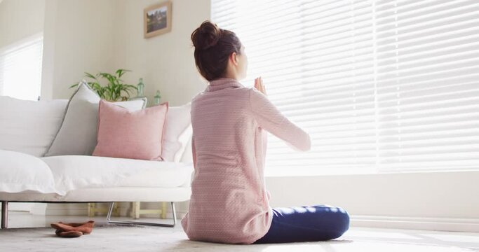 Caucasian woman sitting on floor, practicing yoga and meditating in living room