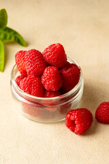 Fresh Raspberry in glass bowl, warm neutral background.