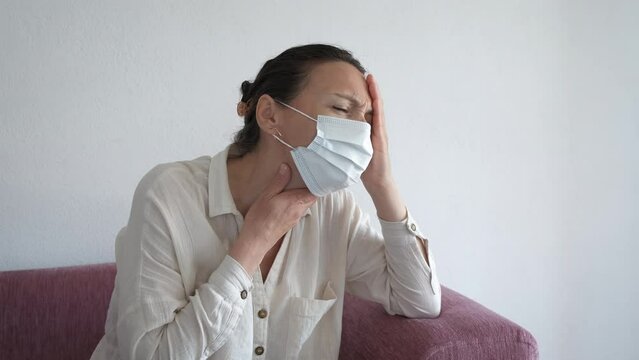 Female suffer from throat ache in mask. A sick female rubbing her neck and suffer from sora throat in protective medical mask indoor.