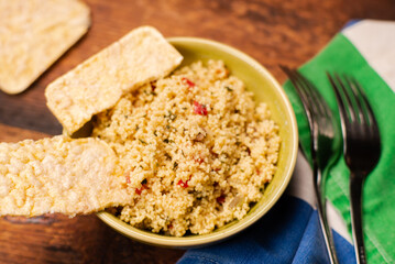 couscous, spices and tomato tabbouleh salad with rice bread in a yellow plate on a wooden background. Traditional oriental salad, appetizer.
