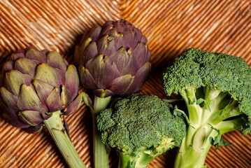 Broccoli and artichokes on a wooden background. Healthy and vegan food. Green cabbage broccoli and purple artichokes.