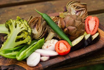 Artichokes, broccoli, onions, tomatoes and various vegetables on a wooden tray. Vegan healthy food, diet concept. Preparing to cook grilled vegetables.