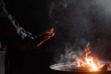 Male hands of an unrecognizable person warm themselves near the fire of a barrel in the dark....