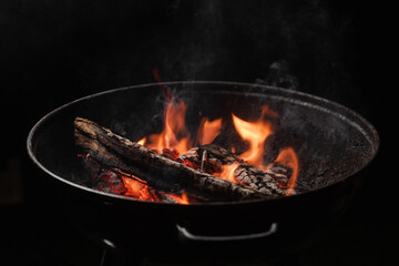 Firewood burns in a round barbecue at night. Dark background. Preparing to cook food on the grill.