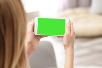 Chroma key compositing. Woman holding smartphone with green screen indoors, closeup. Mockup for design