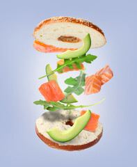 Tasty cut bagel with different ingredients flying on grey background