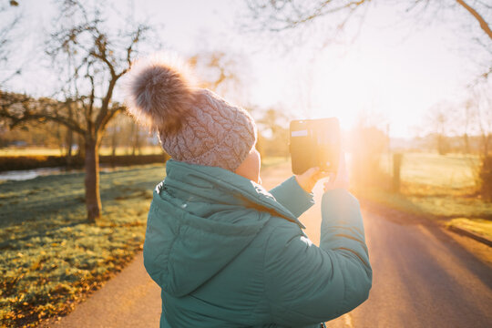 A woman in a knitted hat with a pom-pom takes pictures on a mobile phone, a portrait in golden sunlight, tourism.