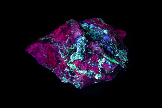 Fluorescent mineral sample under ultraviolet (UL) light displaying bright, various colors. Containing calcite, fluorite, willemite, aragonite. From the Purple Passion mine in Arizona. Black background