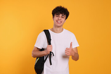 Handsome young man with backpack showing thumb up on orange background