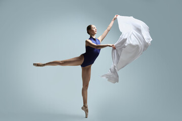 Graceful young ballerina practicing dance moves with veil on grey background