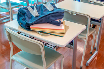 教室の机の上に置かれたスクールバックからはみ出したノートとペンケース。学校生活のイメージ、背景素材 - Powered by Adobe