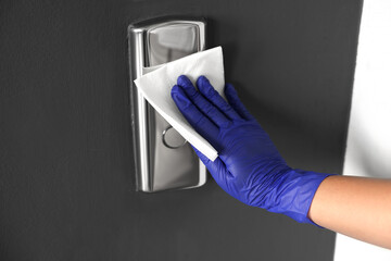 Woman wiping elevator call panel with paper napkin, closeup