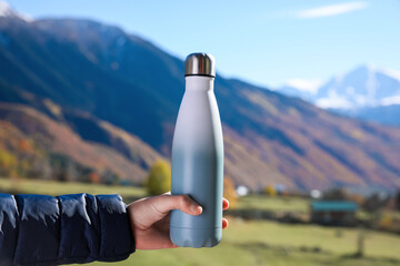 Boy holding thermo bottle with drink in mountains on sunny day, closeup