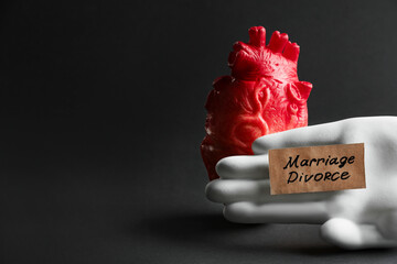 Model of heart, decorative hand and card with words Marriage Divorce on black background, space for...
