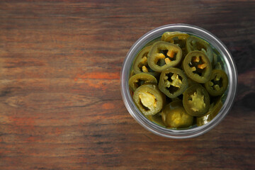 Glass jar of pickled green jalapeno peppers on wooden table, top view. Space for text