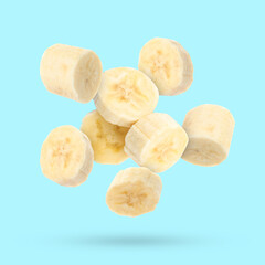 Pieces of delicious ripe banana falling on light blue background