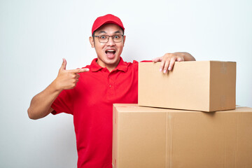 Confident asian courier man in red uniform encourage call service, showing and pointing at cardboard box while lean on it