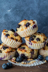 A small pile of freshly made blueberry muffins against a blue background.