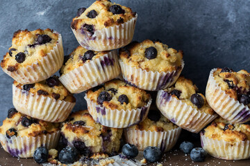 A large pile of homemade blueberry muffins against a blue background.
