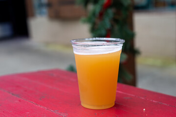 A top-down view of a clear glass of Belgian beer. The creamy carbonated draft head has froth foam and air bubbles of gas rising. The brew ale is on a vibrant red wooden plank table at a microbrewery. 