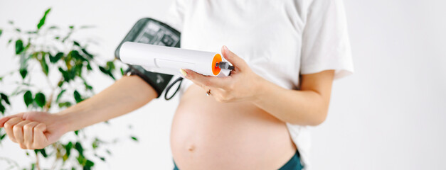Happy pregnant girl sitting on the bed and measures blood pressure and stroking her tummy.