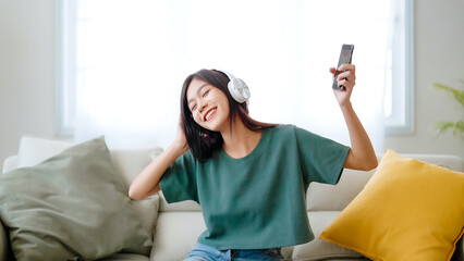 Young asian woman listening to music on couch in living room at home. Happy asia female using...