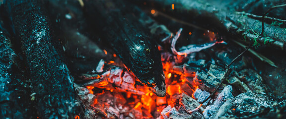 Vivid smoldered firewoods burned in fire close-up. Atmospheric warm background with orange flame of...